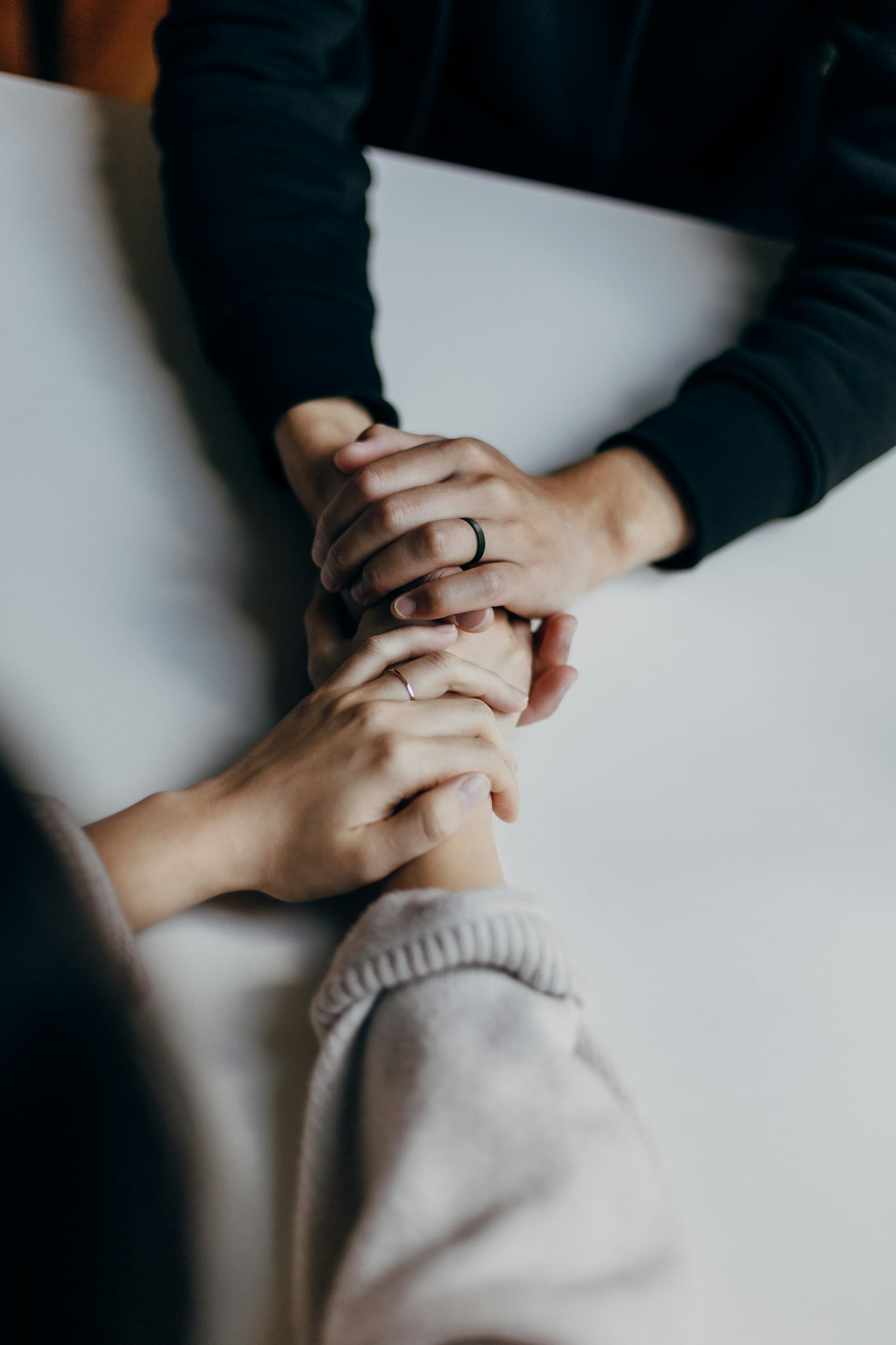 Two people holding hands across a table in a quiet moment of support