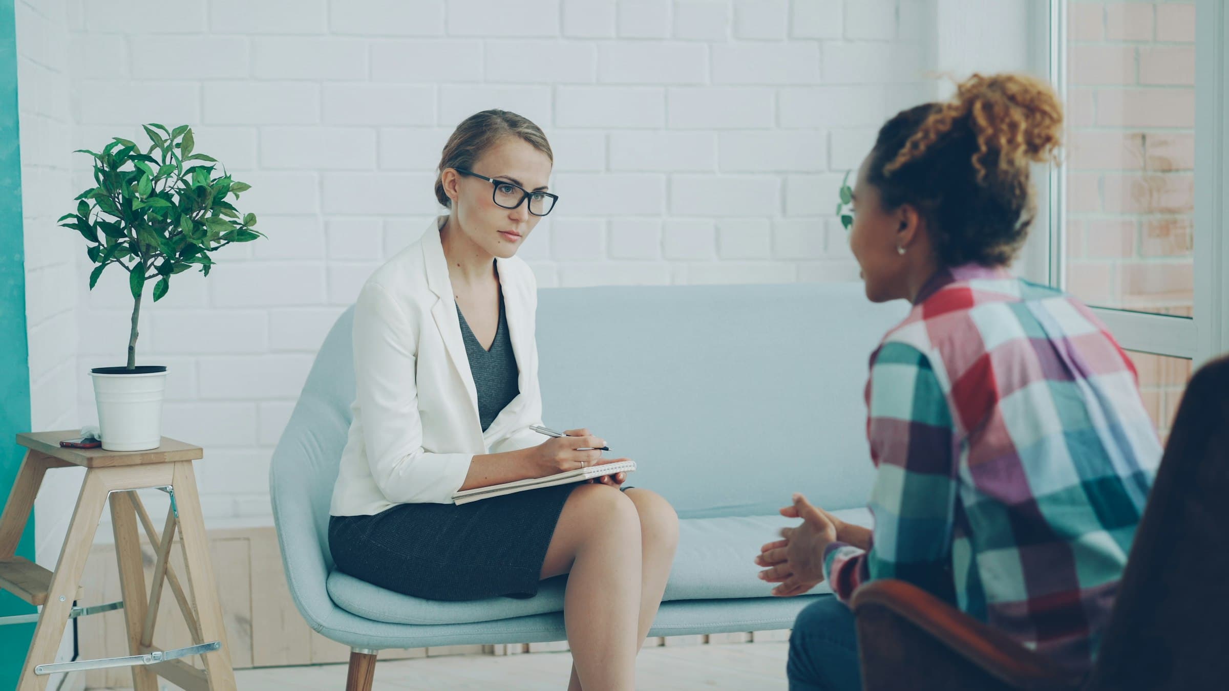 Counselor taking notes while listening to a client in a bright, calm office